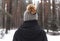 Back of woman in hat with pompom walking on path in snowy forests. Alone person in snow weather