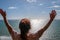 Back of woman with long red hair looking out at a calm flat ocean with her arms up in the air.