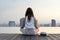 Back of woman relaxingly practicing meditation at the swimming pool rooftop with the view of urban skyline building to attain