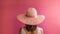 Back of woman wearing wide brimmed sunhat on pink background