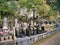 With the backdrop of a rocky outcrop and trees, colourful, flowers adorn well kept gravestones in a cemetery in Japan