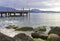 In the background a boardwalk leads into Lake Garda. In the foreground are large pebbles and stones overgrown with algae