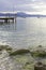 In the background a boardwalk leads into Lake Garda. In the foreground are large pebbles and stones overgrown with algae