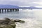 In the background a boardwalk leads into Lake Garda. In the foreground are large pebbles and stones overgrown with algae