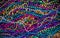 A background of brightly colored Mardi-Gras beads on a purple b