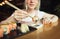 Background. Closeup photo of sushi in chopsticks over a dish with soy sauce, girl sitting at a table in a Japanese restaurant and