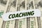 On the background of dollars lies a piece of paper with the text - COACHING