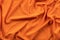 Background in the form of linen fabric of bright orange color with various folds on the material