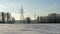 In background high-voltage electricity power pylon on snowy field with trees. High voltage poles on blue sky background