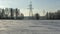 In background high-voltage electricity power pylon on snowy field with trees. High voltage poles on blue sky background