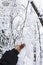 Background man`s hand in a black jacket shakes snow from a snowy tree branch