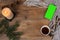 Background with mug of tea, smart phone with blank green screen, candles, knitted shawl with fringe, coniferous branches on wood,