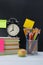 Background of sets of office items and a black alarm clock on colorful books, next to a glass with pencils