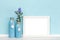 Background template with white wooden horizontal picture frame and vases with flowers in front of blue wall