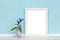 Background template with white wooden vertical picture frame and vase with blue flowers in front of turquoise wall