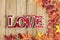 Background texture of old wooden table, yellow autumnal fallen maple leaves, lamp in form of red letters love