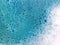 Background with white soap foam in blue turquoise bright water. Ocean or bathroom