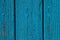 Background of a wooden fence with vertical boards with blue peeling paint close-up, the old door of a village fence