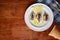 Background of a wooden table top with a plate of baked sardines on it, with bread, cutlery and a napkin on the edge, with space