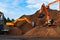 Backhoe standing on big pile of wood chips loading up into truck. Woodchips raw material storing and transportation.