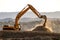 Backlit Backhoe scooping dirt and dust with hills in the background