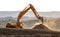 Backlit Backhoe scooping dirt and dust with hills in the background