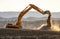 Backlit Backhoe scooping dirt and dust with hills in the background