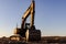 Backlit excavator on an industrial site against the background of the evening sky. Construction machinery for earthworks