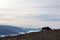 A backlit horse, eating grass, on top of a mountain, with some d