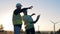 Backlit male energetics workers are having a discussion beside windmills