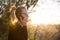 Backlit rear view of young woman talking on cell phone outdoors in park at sunset. Girl holding mobile phone, using