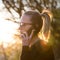 Backlit rear view of young woman talking on cell phone outdoors in park at sunset. Girl holding mobile phone, using