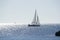 Backlit sailboat on bright and sunny sea with horizon