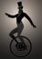 Backlit silhouette of equilibrist dressed in the old fashion, wearing top hat, balancing on unicycle