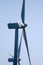 Backlit view of blades, rotor hub and nacelle of two wind mills and blue sky in the background.