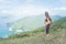 Backpack female traveler standing on hill looking at sea and mountains. Trail runner taking a break enjoying view of