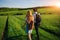 With a backpack, a man in a hat and a woman with long hair go along the path. A couple walks along the meadow