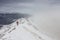 Backpacker climbing a mountain narrow snowy ridge in winter