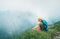 Backpacker man has a rest break enjoying cloudy valley bottom walking by the foggy cloudy weather mountain range . Active sports