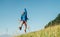 Backpacker traveler emotionally jumping over green grass mountain meadow with backpack with wide opened arms and legs. Human`s