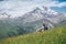 Backpacker woman sitting on a green grass hill and enjoying snowy slopes of Kazbek 5054m mountain with a backpack while she