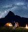 Backpackers girl and guy looking at the shines starry sky at night. Young couple sitting near tent and campfire