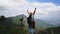 Backpacking female hiker stands on top of the mountain with raised arms and enjoying the view. journey and success concept