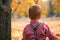 Backside of child boy playing in autumn city park. Bright yellow trees and leaves