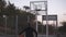 Backside footage of a young basketball female player jogging with ball on the outdoors court and throw it to the hoop