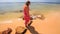 Backside Girl in Long Walks Barefoot along Sea on Sand Beach