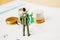 backside of miniature business man with blurred green thumbtack and stack of coins on calendar