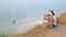 Backside view cute positive blonde girl and brunette girl sit on edge of cliff and take selfie pictures with help phone