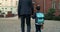 Backside view of man in suit waiting for son while standing at yard. Little child with backpack taking his father hand