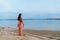 Backside view slim girl with long hair in sundress with bag on long strap walks at sandy tropical beach